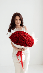 Woman in white dress holding large bouquet of fresh red roses with white wrapping and red ribbon