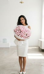 Woman holding a large bouquet of pink flowers in a minimalistic room.