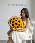 Woman in white dress holding bouquet of sunflowers, elegant floral arrangement indoors