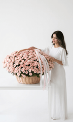 Woman in white dress with large basket of pink roses on white table, elegant floral arrangement
